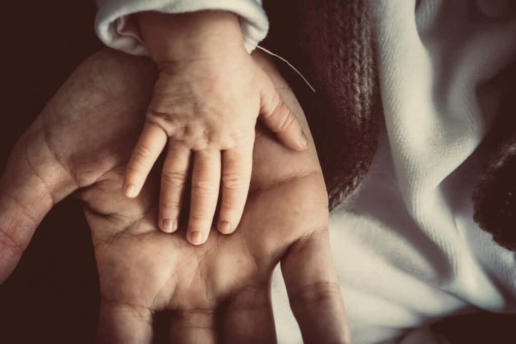 A child's hand on an adult's hand. An adult is a smarter child, but still a child deep down. To act like an adult means to act like a child sometimes. 