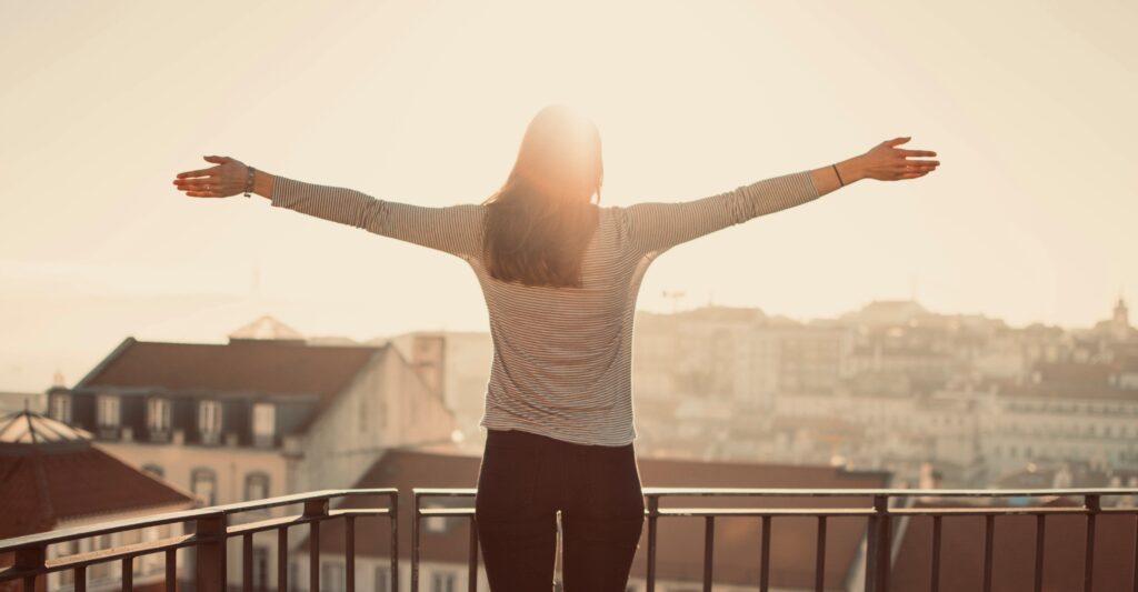 Morning sunshine. Woman in the balcony spreading her arms wide towards the sun. 