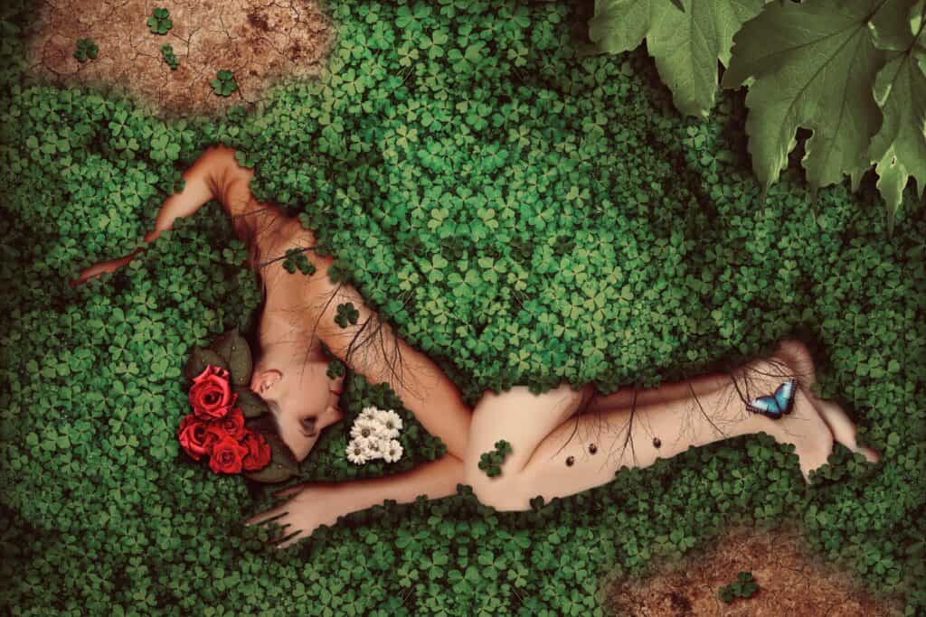 Naked woman lying on the grass. Half of her body is covered by leaves and flowers. 