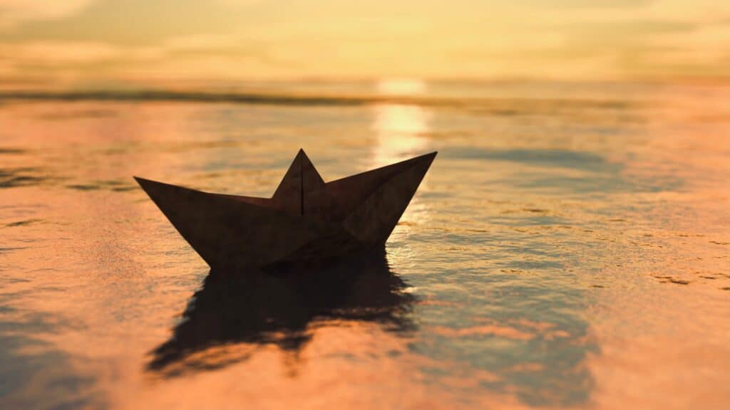 origami boat floating on beach shore at sunset.