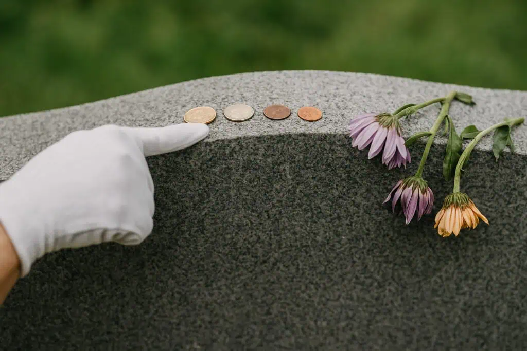 Gloved hand and four coins on headstone